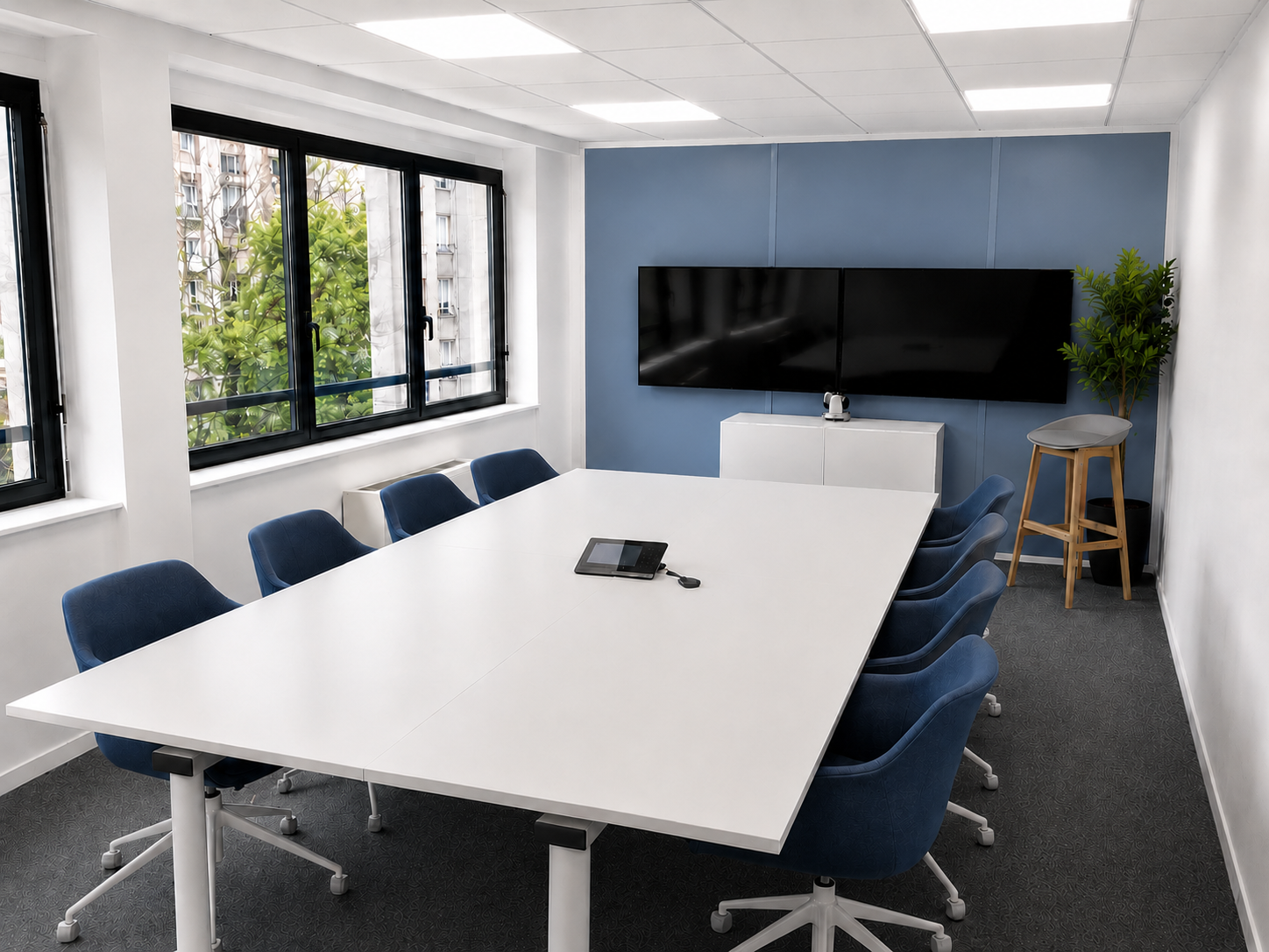 Salle de réunion équipée d'une table blanche, de fauteuils bleus et d'écrans muraux